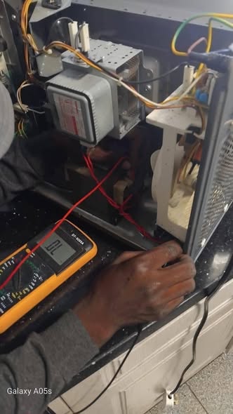Technician checking voltage with a multimeter inside a microwave